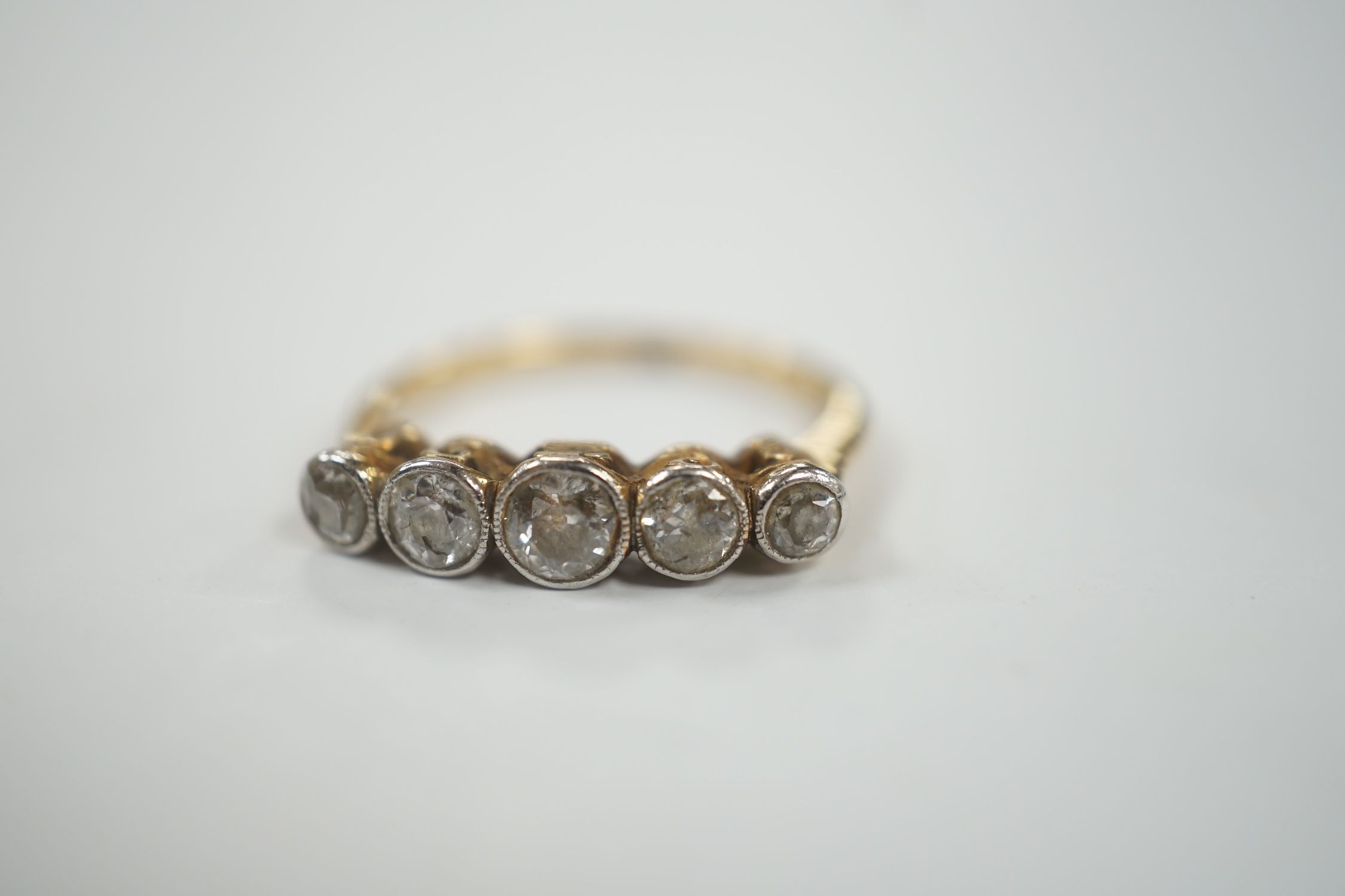 A yellow metal (stamped 18) and graduated five stone diamond set half hoop ring, size M/N, gross weight 3 grams.